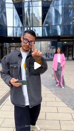 a man standing in front of a tall building giving the peace sign with his fingers