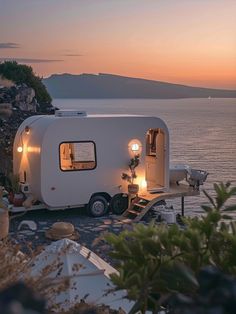 an rv is parked on the shore at dusk with its lights on and it's door open