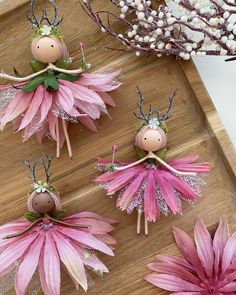 four pink flowers and three wooden fairy dolls on a wood tray next to some twigs