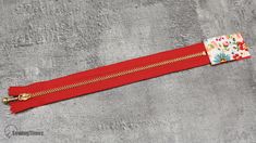 a red zipper with flowers on it and a gold metal hook hanging from the end