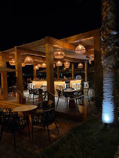 an outdoor dining area at night with lights hanging from the ceiling and wooden tables and chairs