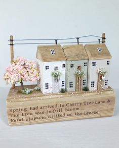 a wooden box with three small houses on it and flowers in the window sill