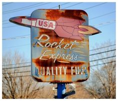 an old rusty rocket engines sign on top of a blue pole with power lines in the background