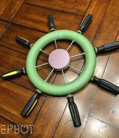 a green steering wheel with black handles on a wooden floor, surrounded by screwdrivers