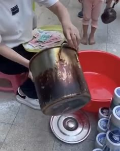 a man is pouring water into a bucket on the ground next to other cans and cans