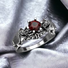 a red stone ring sitting on top of a silver cloth