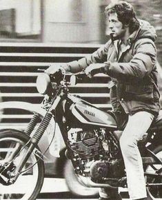 a man riding on the back of a motorcycle down a street next to some stairs