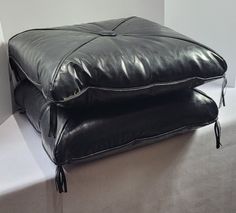 two black leather pillows sitting on top of each other in front of a white wall