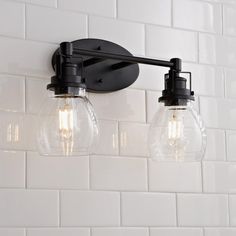 two light fixtures mounted on a white tile wall in a bathroom with black fittings