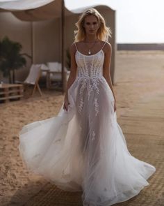 a woman is walking on the beach in a white wedding dress with an open back