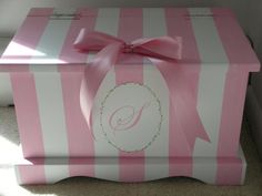 a pink and white striped box with a bow on the top that has a monogrammed initial