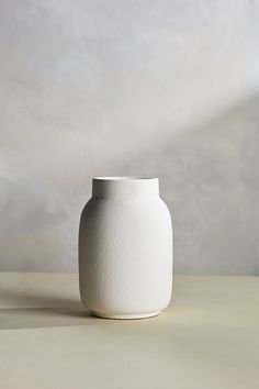 a white vase sitting on top of a table next to a wall in the background