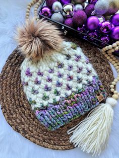 a knitted hat sitting on top of a woven mat next to purple and white ornaments