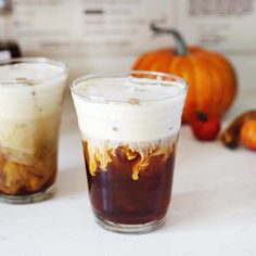 two glasses filled with liquid sitting on top of a table next to some pumpkins