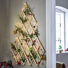 a christmas tree made out of wooden sticks and ornaments hanging on the wall next to a window