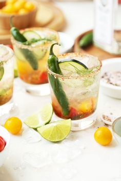 two glasses filled with drinks sitting on top of a table next to lemons and limes