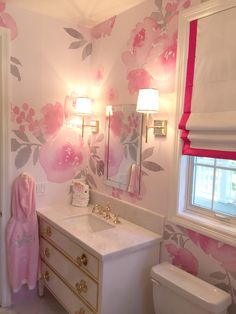 a bathroom decorated in pink and white with flowers on the wall behind the sink, toilet and mirror