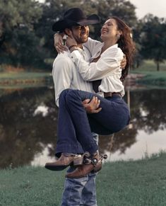 a man riding on the back of a woman's shoulders in front of a pond