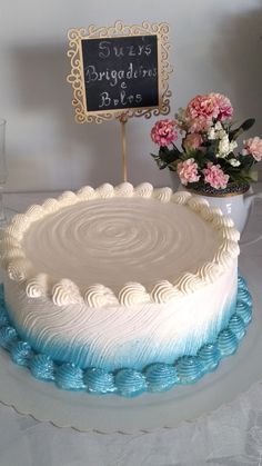 a white cake with blue icing and flowers on the table next to a sign