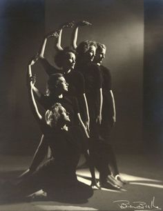 an old black and white photo of four women posing in front of the camera with their arms up