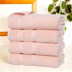 six folded pink towels sitting on top of a white counter next to a potted plant