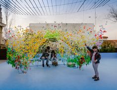 two people standing in front of an art installation made of plastic bottles and streamers