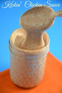 a spoon sticking out of a jar filled with chicken sauce on top of an orange napkin