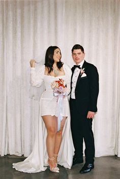 a bride and groom pose for a photo in front of a white curtained backdrop