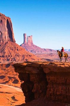 a man riding a horse on top of a rocky cliff in the middle of desert