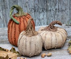 two small pumpkins sitting next to each other on a wooden surface with leaves and acorns