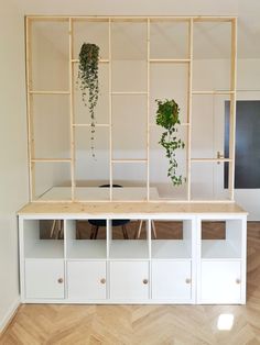 a room with white shelves and plants on top of them, along with a wooden floor