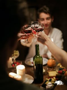 two people toasting wine glasses over a table with cheese, fruit and candles on it