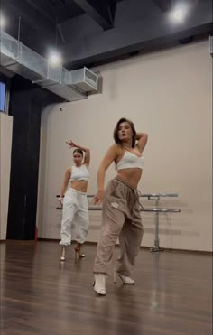 two women in white top and tan pants dancing on wooden floor with lights above them