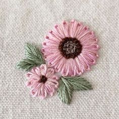 two pink flowers with green leaves are on a white surface, and one is embroidered onto the fabric