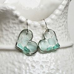 a pair of glass heart shaped earrings sitting on top of a white vase