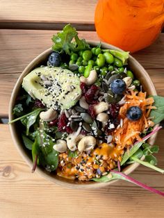 a bowl filled with vegetables and fruit on top of a wooden table next to an orange pumpkin