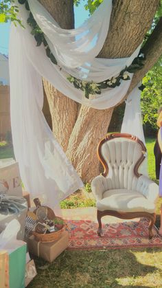 an old chair sitting under a tree in front of a white drape covered canopy