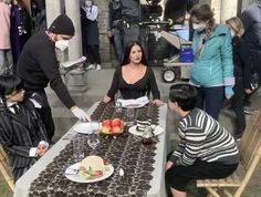 a group of people sitting around a table with food on it and masks covering their faces