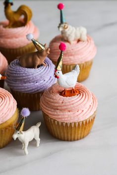 cupcakes with pink frosting and small animals on top are arranged in rows