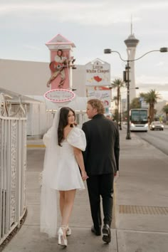 a bride and groom walking down the sidewalk in front of a neon sign that reads las vegas