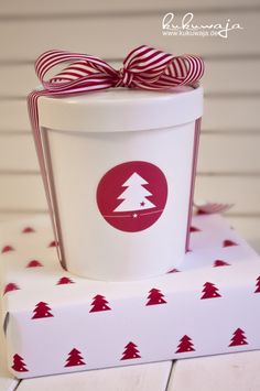 a white cup sitting on top of a red and white box with a bow around it