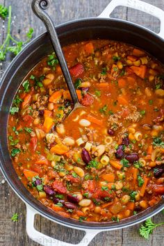 a pot filled with soup and vegetables on top of a wooden table next to some parsley