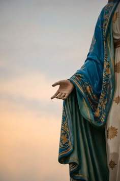 the statue is wearing a blue robe and holding his hands out to the sky with clouds in the background