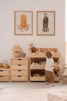 a little boy standing in front of a wooden dresser with two pictures on the wall