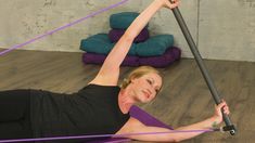 a woman is doing exercises on the floor with a resistance band in her hand and holding onto an exercise pole