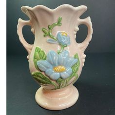 a white vase with blue flowers painted on the side and green leaves in the middle