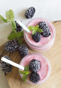 two glasses filled with smoothie and blackberries on top of a wooden cutting board