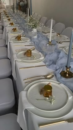 a long table is set up with white plates and silverware for an elegant dinner