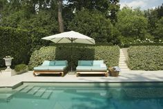 two chaise lounges with an umbrella next to a swimming pool