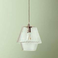 a clear glass light fixture hanging from a metal cord on a green wall background with an empty space for text